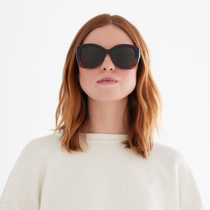Woman wearing large round sunglass that is black on the top and tortoise on the bottom. 